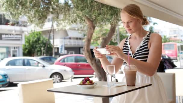 Mujer atractiva tomando fotos de una pastelería en su teléfono inteligente mientras se sienta en una mesa — Vídeos de Stock