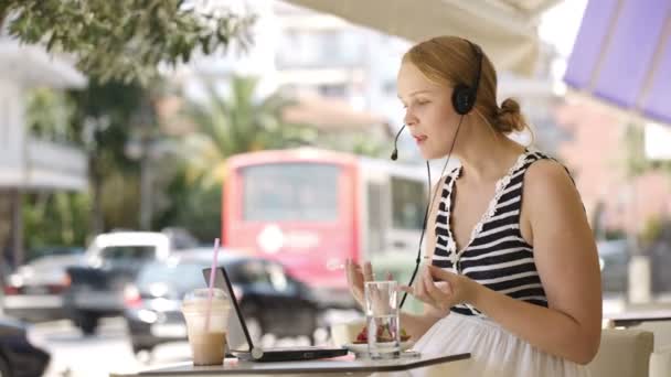 Mulher loira atraente sentada com um laptop em um restaurante ao ar livre conversando com sua amiga usando skype — Vídeo de Stock