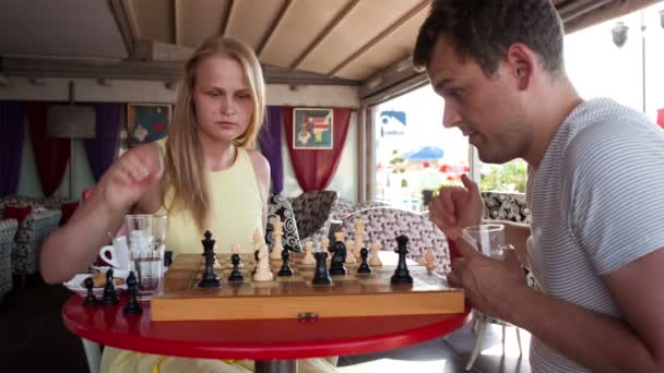 Lächelndes Paar beim Schachspiel, während es an einem Tisch sitzt und einen Drink genießt — Stockvideo