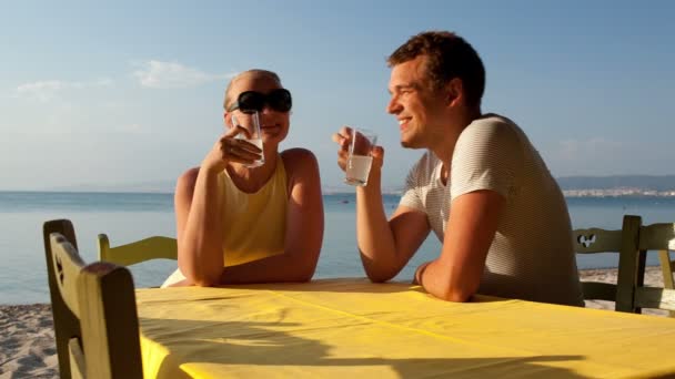 Pareja joven disfrutando de bebidas en la playa — Vídeo de stock