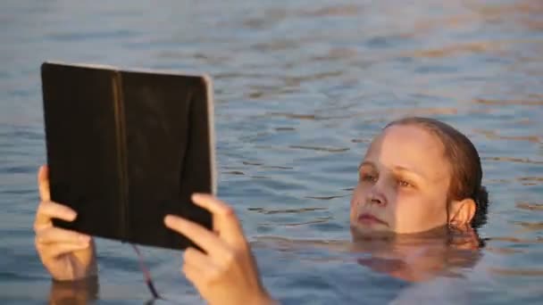 Young woman reading a book in a calm sea — Stock Video