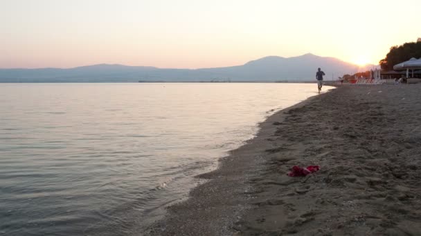 夜明けに太陽とトロピカル ビーチに沿って走る男 — ストック動画