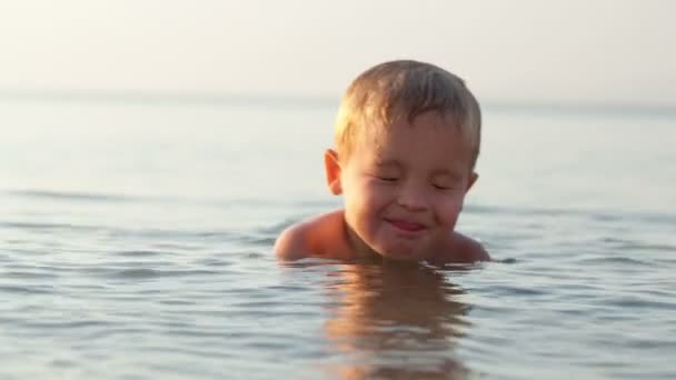 Leende liten pojke smiter ner i grunt vatten vid havet — Stockvideo