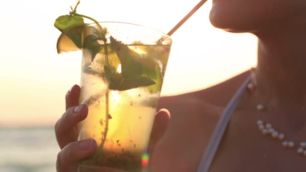 Gros plan d'une femme dégustant un cocktail de mojito tropical décoré de fruits frais au bord de la mer — Video