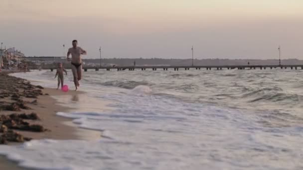 Vader en zijn zoontje loopt langs het strand spelen bal — Stockvideo