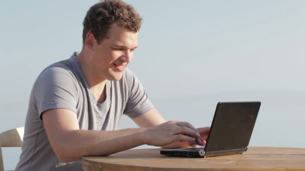 Hombre escribiendo ordenador portátil disfrutando del sol de verano mientras está de vacaciones — Vídeos de Stock