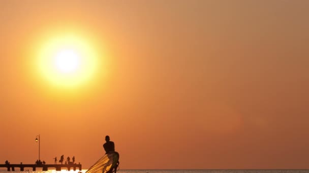 Uomo che alza il suo windsurf o tavola a vela al tramonto — Video Stock