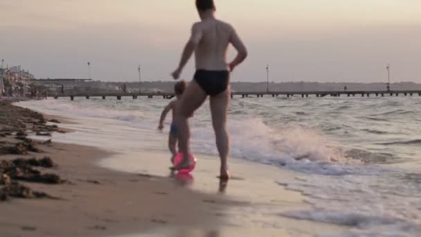 Padre y su hijito corriendo por la playa jugando a la pelota — Vídeo de stock