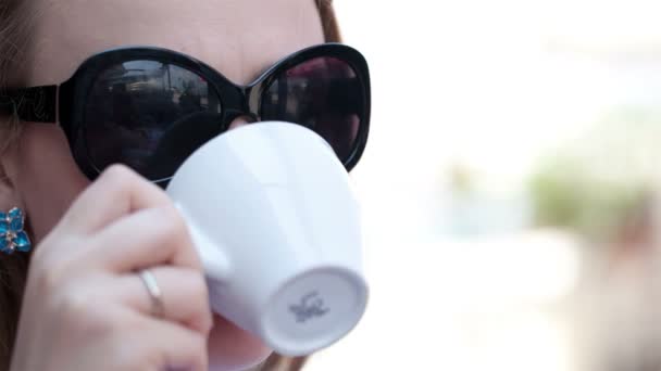 Mujer joven en gafas de sol bebiendo café en la cafetería de la calle — Vídeos de Stock