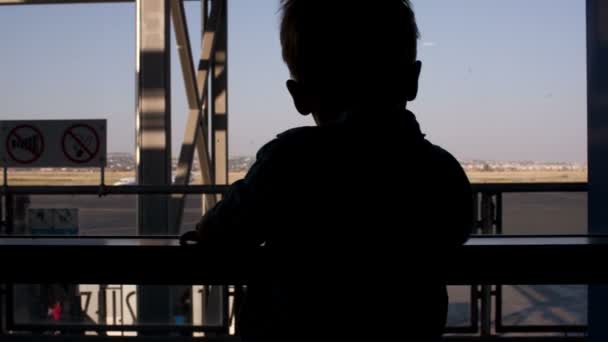 Silhouette eines kleinen Jungen, der durch ein Fenster im Flughafen blickt — Stockvideo