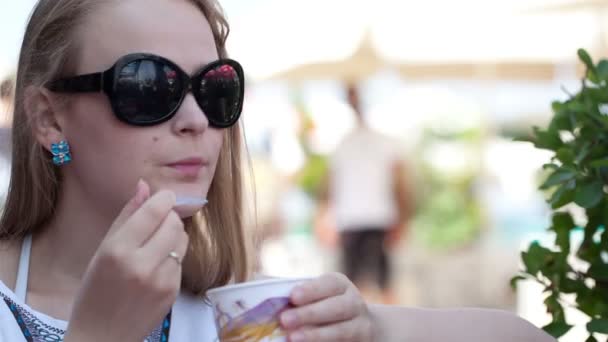 Jonge vrouw in zonnebril eten van ijs in de straat café — Stockvideo