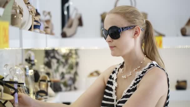 Young woman in sunglasses choosing summer shoes in the shop — Stock Video