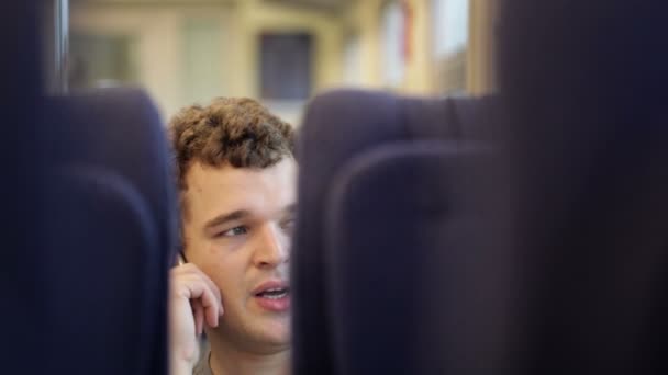 Молодой человек разговаривает по телефону в движущемся поезде — стоковое видео