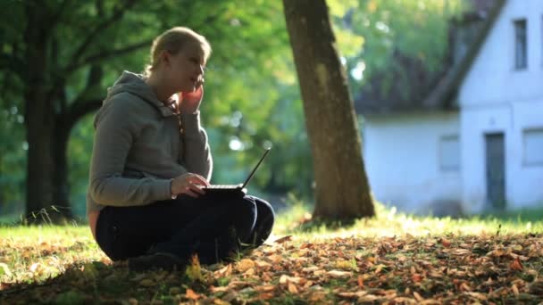 Ung kvinna sitter på marken utomhus med en bärbar dator — Stockvideo