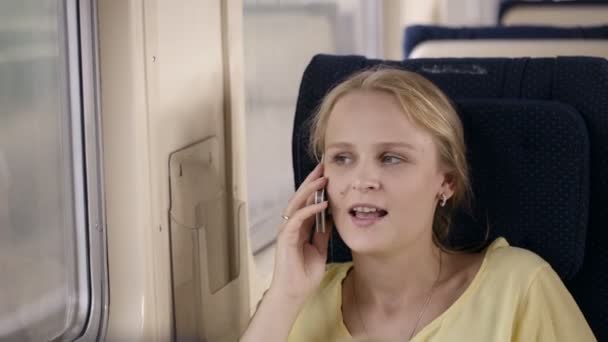 Mladá žena mluví po telefonu ve vlaku a při pohledu z okna — Stock video