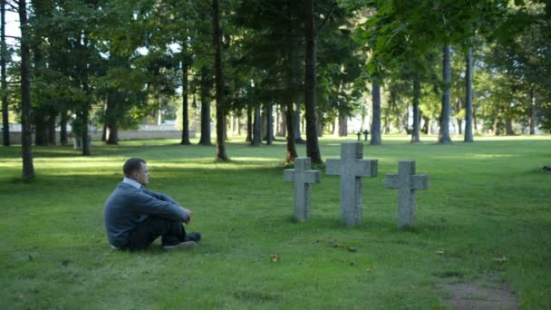 Mann sitzt trauernd vor drei Kreuzen — Stockvideo