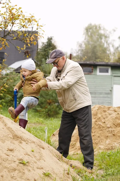 Grandpa helps grandson to get on a sand hill — Stock Photo, Image