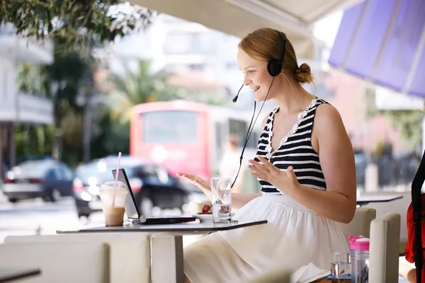 Mujer riendo usando un auricular en la cafetería al aire libre —  Fotos de Stock