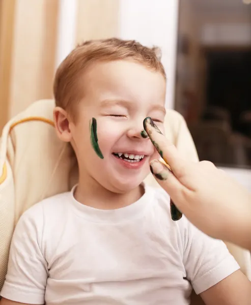 Pequeño niño riendo mientras su madre le pinta la cara — Foto de Stock