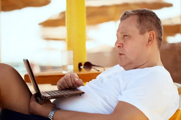 Мужчина отдыхает с ноутбуком на пляже курорта — стоковое фото
