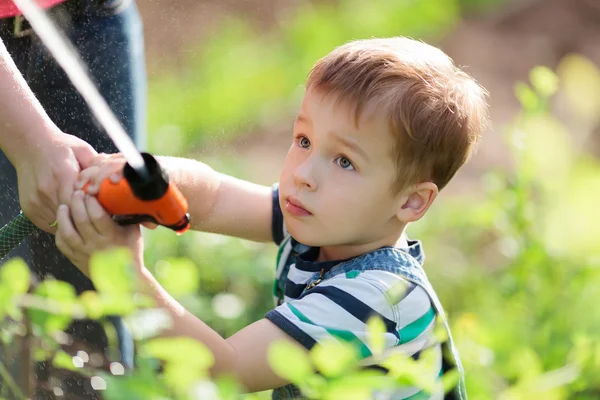 Kleiner Junge spielt mit einem Wasserstrahl im Garten — Stockfoto