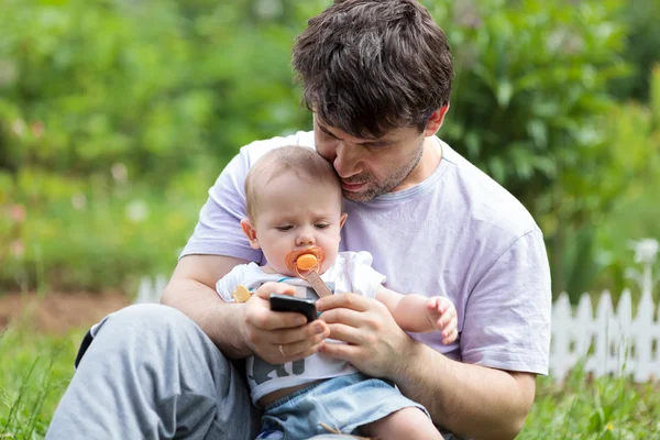 Pai segurando um bebê e mensagens de texto em seu celular — Fotografia de Stock