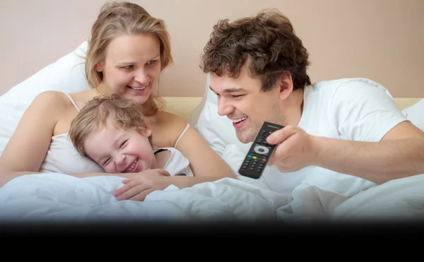 Счастливая семья лежит в постели и смотрит телевизор — стоковое фото