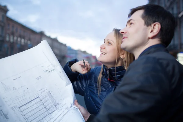 Couple holding blueprints admiring building — Stock Photo, Image