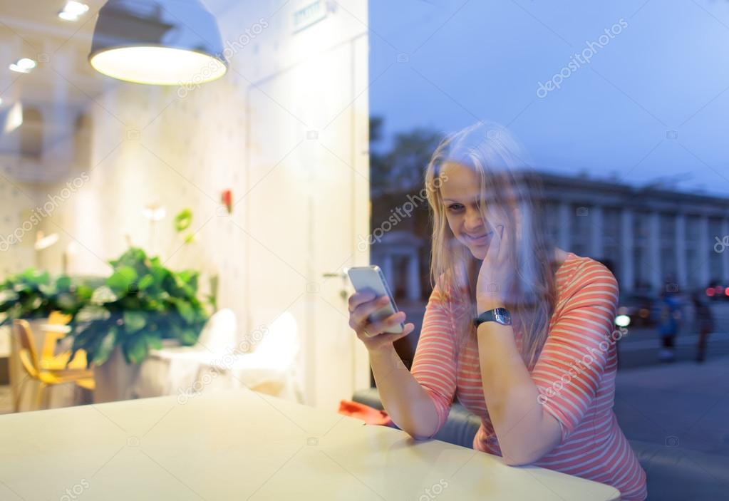Smiling woman in cafe reading or typing sms