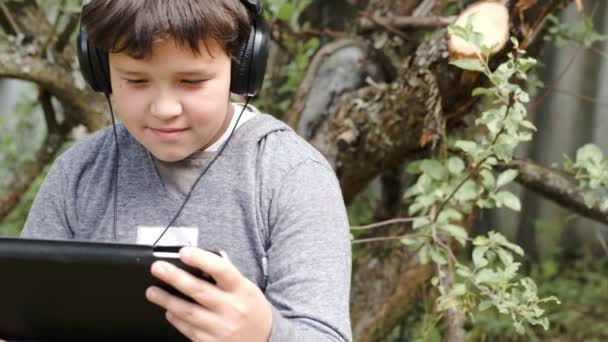 Menino em fones de ouvido com touchpad ao ar livre — Vídeo de Stock