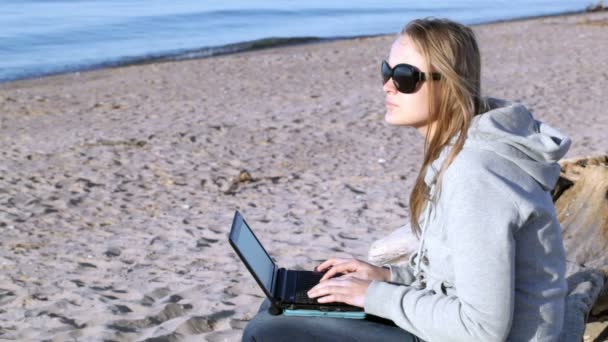 Mujer en gafas de sol usando portátil en la playa — Vídeos de Stock