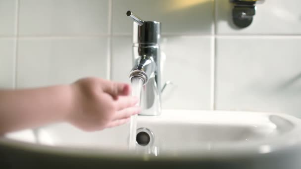 Childs Hand berührt Wasser, das aus dem Wasserhahn strömt — Stockvideo