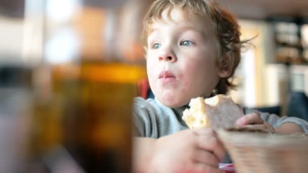 Милый мальчик ест булочку в кафе — стоковое видео