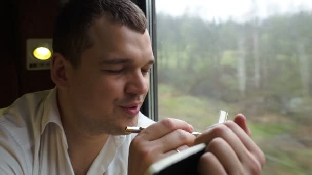 Jeune homme réfléchi prenant des notes dans le train — Video