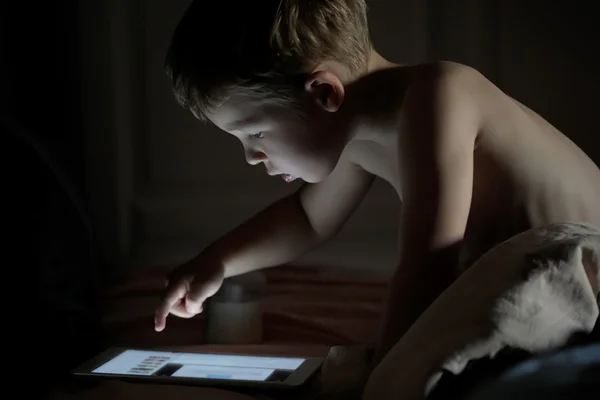 Маленький мальчик, использующий планшетный компьютер ночью — стоковое фото