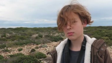 Vahşi doğaya ve gökyüzüne karşı ceketli bir çocuğun portresi. Genç turist ve kaşif, rüzgar saçlarını dalgalandırıyor.