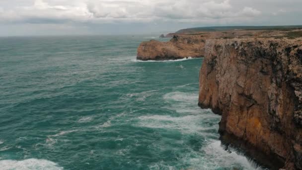 ポルトガルのセントビンセント岬の急峻な岩をクラッシュする紺碧の波の息をのむような風景 雲に覆われた岬と大西洋の自然風景 — ストック動画
