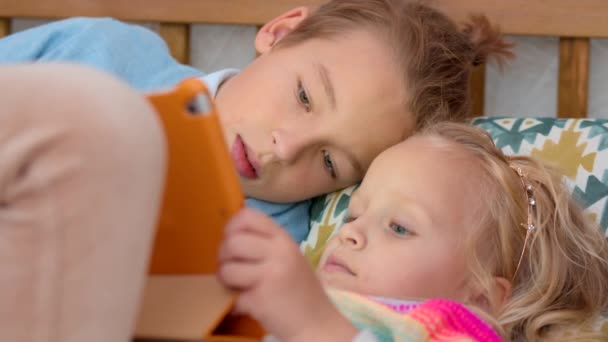 兄と妹はガジェットで暇を過ごしていた 小さな女の子はデジタルタブレットでゲームをプレイし 男の子は見て 時には彼女を助ける — ストック動画