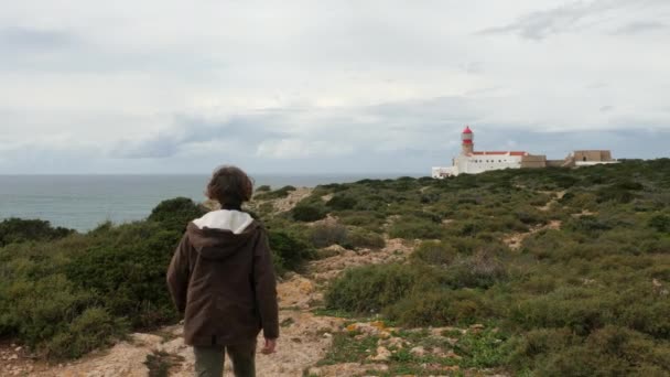 10代の少年は 大西洋を見下ろすセントビンセント岬灯台への岩の道に沿って自分の道を作っています ポルトガルの若い観光客の観光スポット — ストック動画