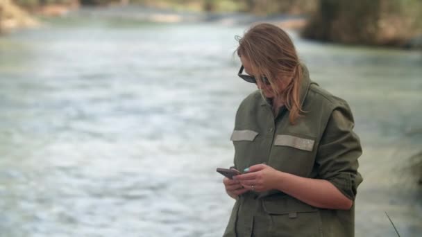 Pirang Kaukasia Dalam Jaket Khaki Kacamata Hitam Berdiri Tepi Sungai — Stok Video