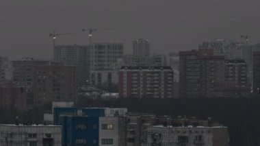 Yapı vinçleri, ışıklarla aydınlatılmış, akşam kentinde, çok katlı konutların arka planına karşı.
