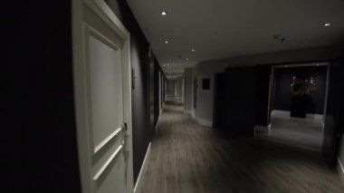 Boş bir otel koridorunda yapay ışıklandırmayla karanlık ve açık renkli iç mekan görüntüsü. Koyu gri duvarlı beyaz kapılar. Konforlu konaklama