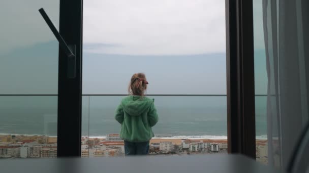 バルコニーからホテルと海とビーチを見て女の子のバックビュー 海岸に住んで休暇を過ごす ポルトガルのナザレ — ストック動画