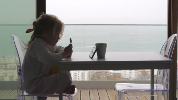 Κοριτσάκι Κουτάλι Βλέποντας Κινούμενα Σχέδια Στο Smartphone Και Περιμένοντας Πρωινό — Αρχείο Βίντεο