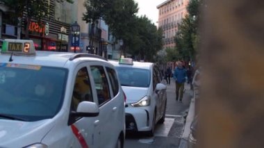 MADRID, İSPAN - 07 Mayıs 2022: şehir caddesinde ulaşım trafiği. Dar yolda taksiler, arabalar ve bisikletler. İnsanlar kaldırımda mağaza afişleriyle yürüyorlar.