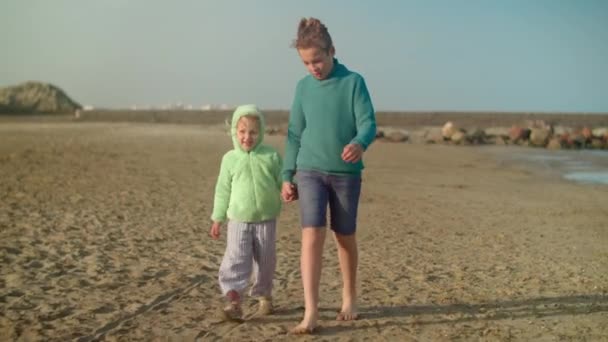 Adolescente Caminando Con Hermana Pequeña Playa Día Fresco Niños Tomados — Vídeos de Stock