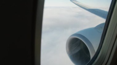 Gökyüzü ve bulutlar görünüyor, bir jet motoru varış noktasına uçan ticari bir uçağın penceresinin dışında.