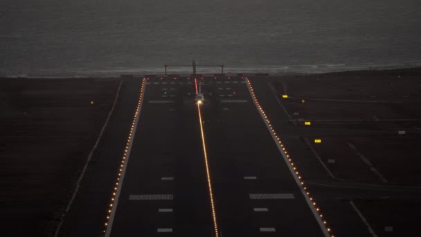 フロントビュー 航空機は明るいヘッドライトと 水の端から始まるライトアップ滑走路で夕方に離陸します — ストック動画