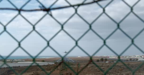 飛行場のフェンスの金属格子を通して撮影された空とワイヤーフェンスの背景に高度を得ている旅客機 — ストック動画