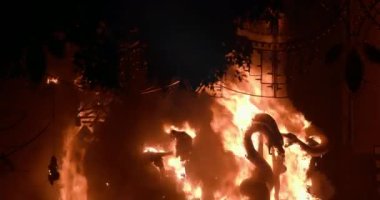 Celebrating traditional Fallas festival and ninot in blazing flames. People looking at burning installation which falling apart